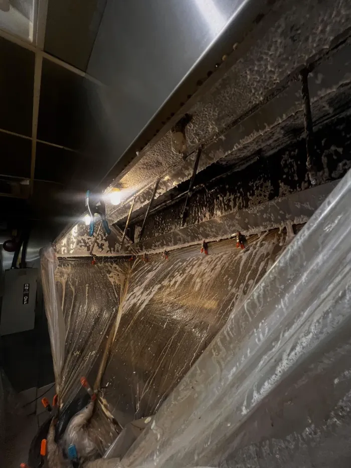 Inside of a kitchen hood coated in grease, wrapped in plastic during cleaning